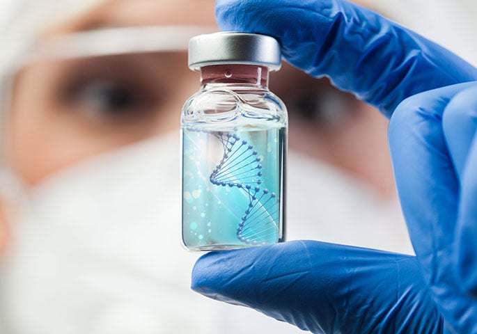 A person wearing protective clothing holds a small glass vial containing a liquid with a graphical representation of a DNA helix.