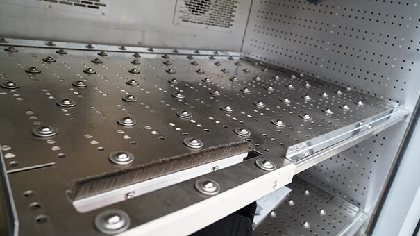 Bandejas para cargas pesadas con rodillos de bolas y un cepillo en un armario climatizado con ventiladores en la pared trasera.