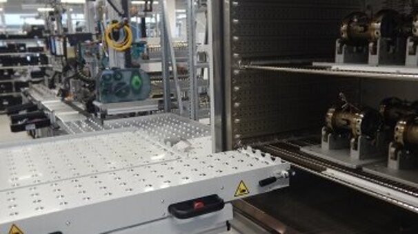 Planta de producción industrial con una cabina de pruebas abierta en primer plano, en la que se encuentran piezas de trabajo. Hay una rampa de acceso delante de la cabina de pruebas.