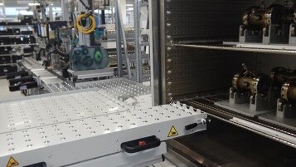 Przemysłowa linia produkcyjna z otwartą szafą testową na pierwszym planie, w której znajdują się elementy. Przed szafą testową znajduje się podnośnik.